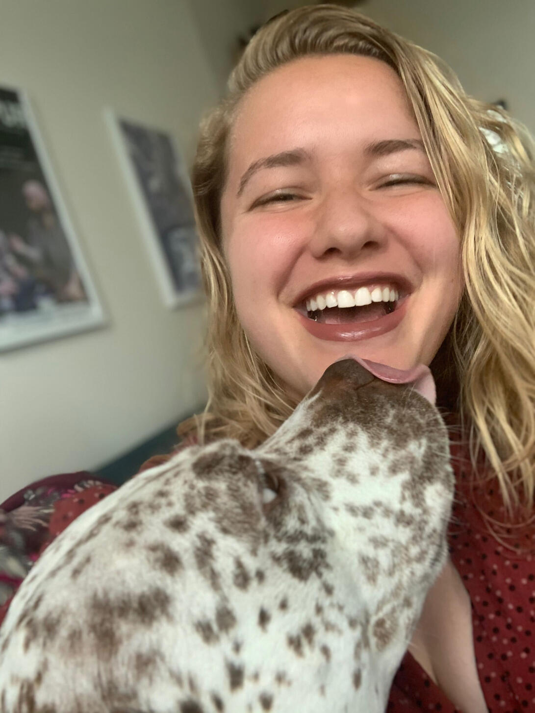 Lelaina, a blonde white woman, smiles as her dog Honey, a pitbull, tries to lick her face.